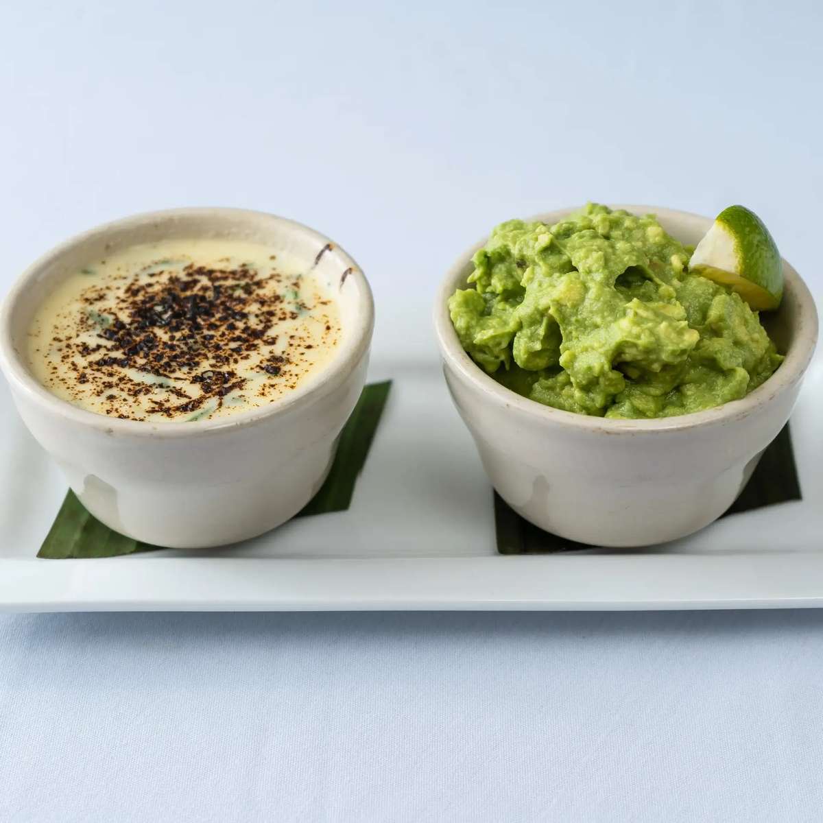 Creamy queso and fresh guacamole served side by side at Mesero on a white plate with a lime wedge.