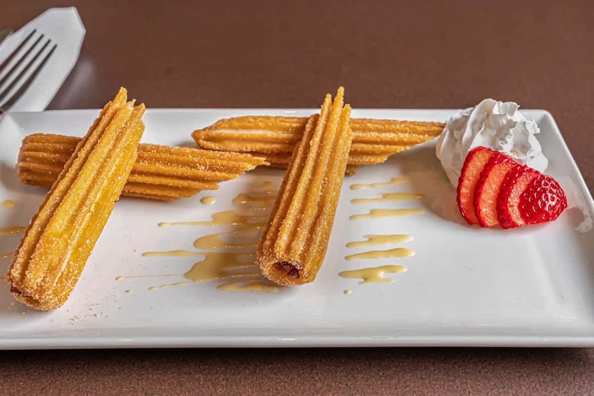 Crispy churros with whipped cream, strawberries, and caramel drizzle served at Mesero.