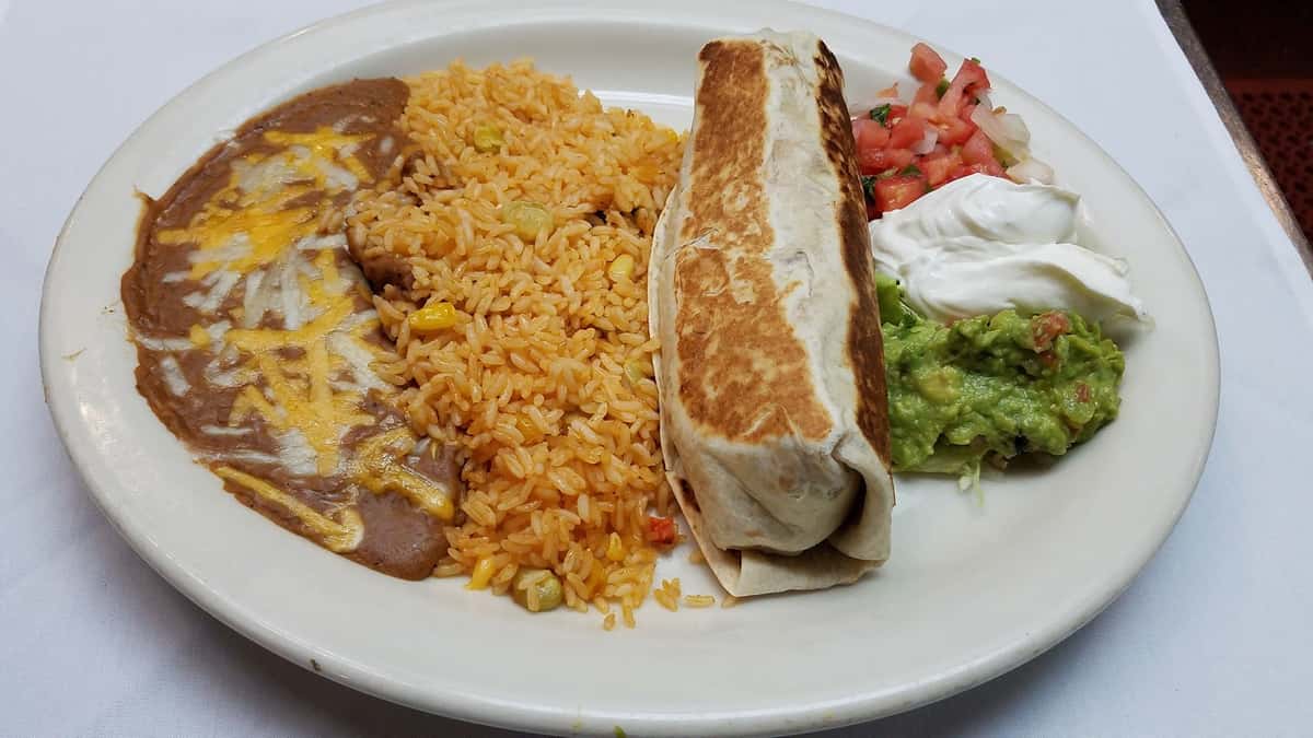 A flour filled tortilla served with yellow Mexican rice, refried pinto beans, lettuce, pico de gallo, guacamole, and sour cream