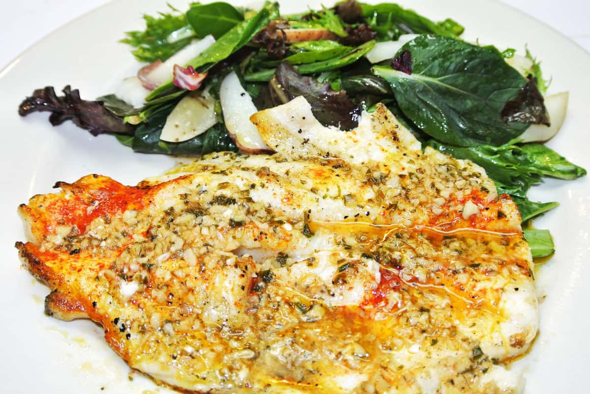 Cooked filet of fish with a garlic sauce and a side of salad