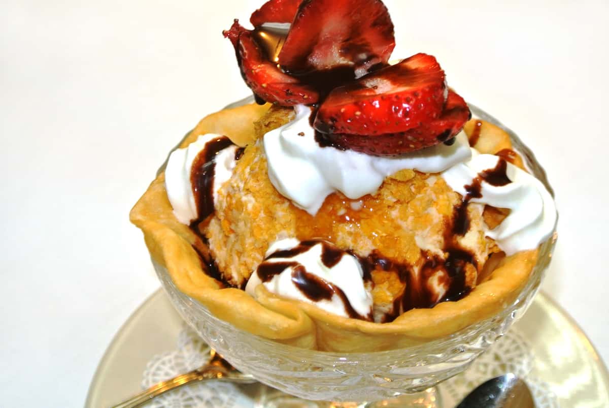 Fried ice cream topped with whipped cream and strawberries with a chocolate drizzle