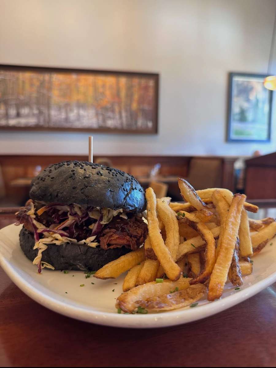 Burger on a dark bun with slaw, served with golden French fries.