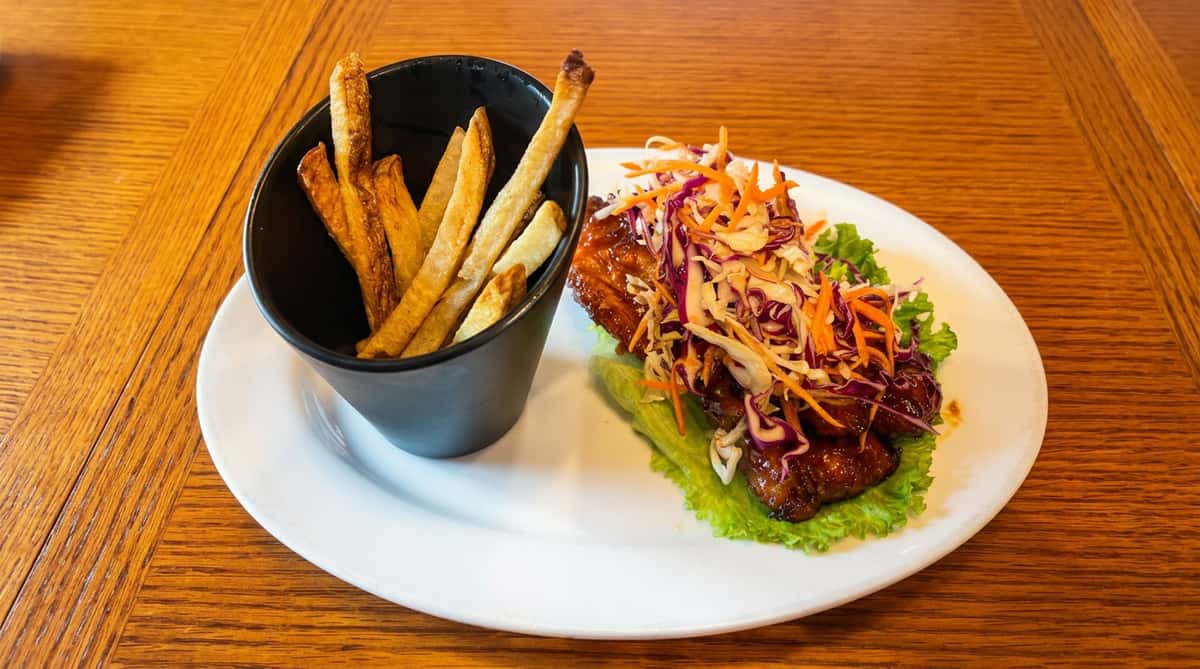 Shiny glazed pork ribs on lettuce with coleslaw, alongside a black cup of french fries.