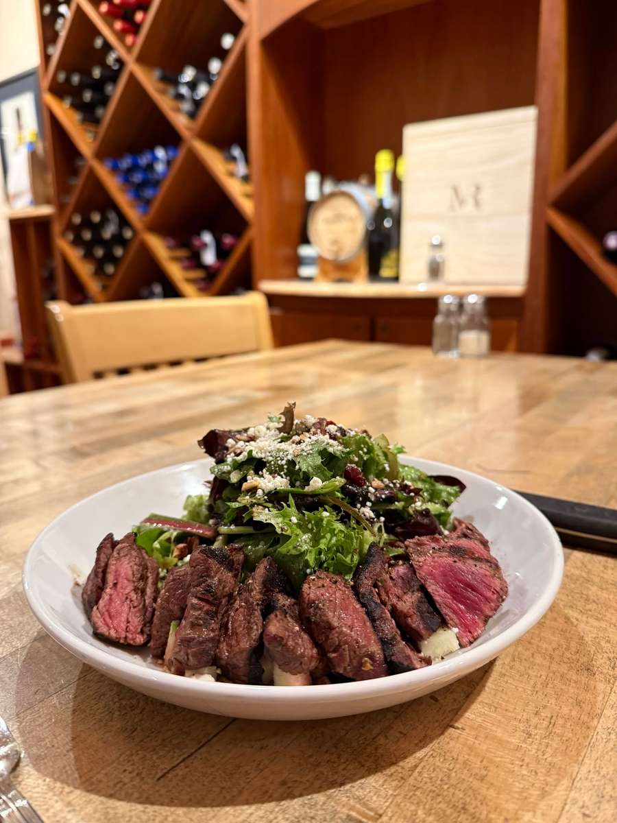 Medium-rare sliced steak served with mixed greens and grated cheese on a white plate.
