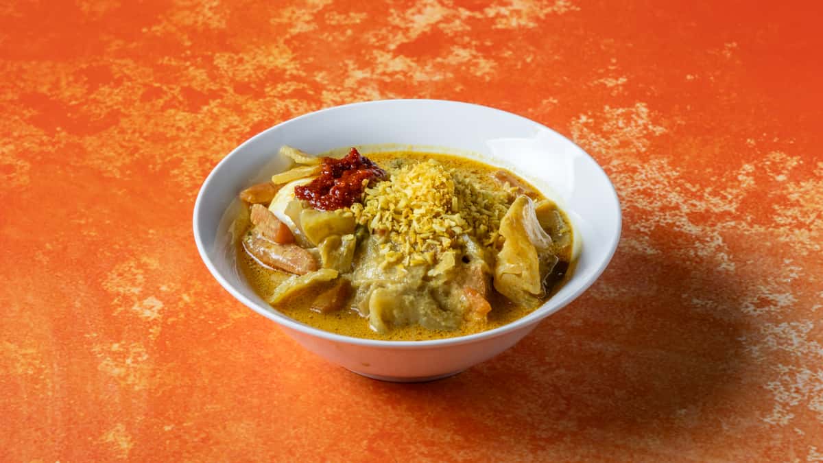 Authentic Malaysian lontong with rice cakes, vegetable curry, shredded coconut, and savory gravy served in a traditional bowl.