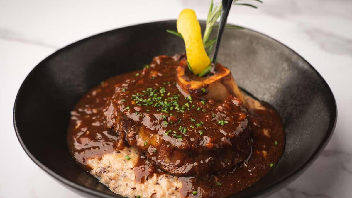 Veal osso buco over Jimmy Red grits in a black bowl on white marble at 360 Bistro, Nashville