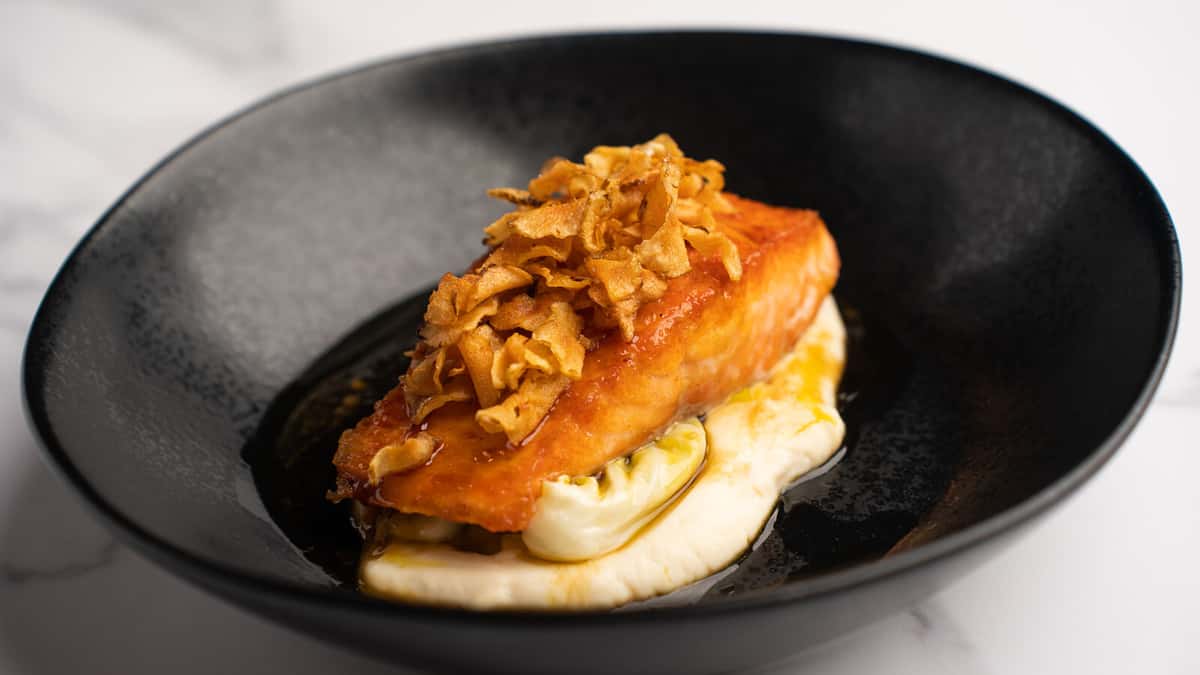 Pan seared Scottish salmon with crispy sunchokes over celery root purée and winter cabbage in a black bowl at 360 Bistro
