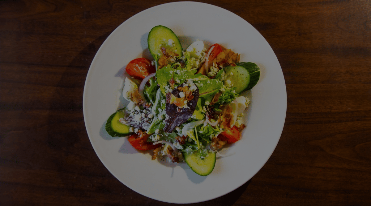 Mixed green salad with cucumbers, tomatoes, hard-boiled egg, red onion, bacon bits, and crumbled feta cheese.