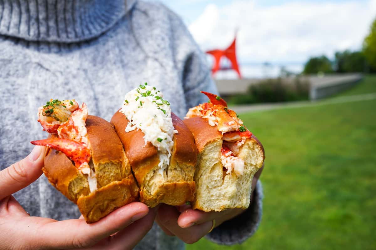 person holding three lobster rolls