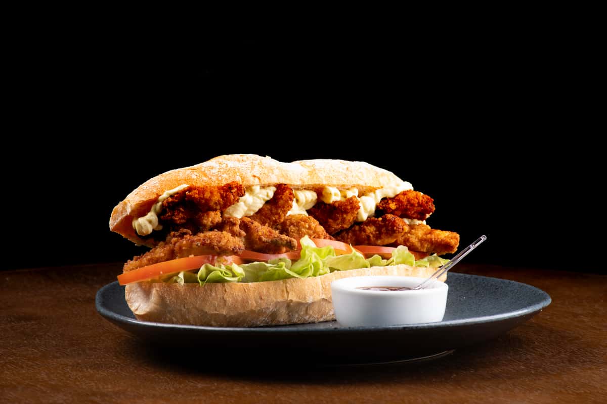 Sub style fried chicken sandwich on a plate with lettuce and tomato, with a small cup of dipping sauce