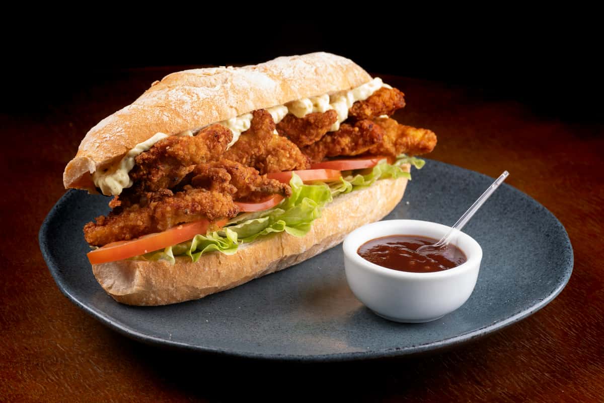 Large fried sandwich on a plate with lettuce and tomato, with a small cup of dipping sauce
