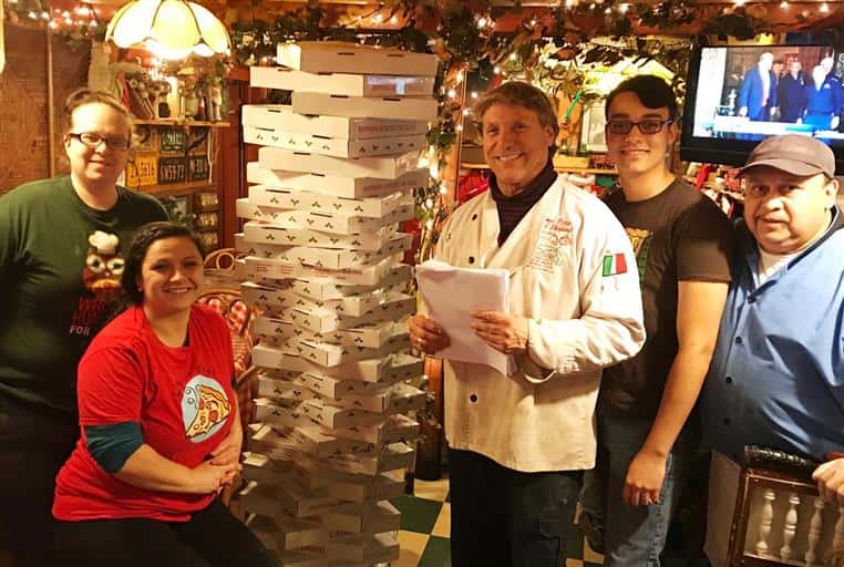 Prima Pizza family and staff posing near stacked pizza boxes.