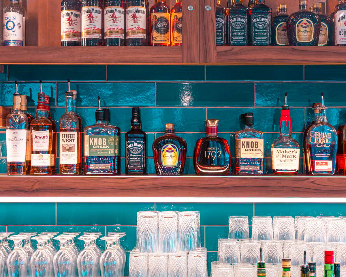 Row of liquor bottles lined up on a shelf against a teal wall.