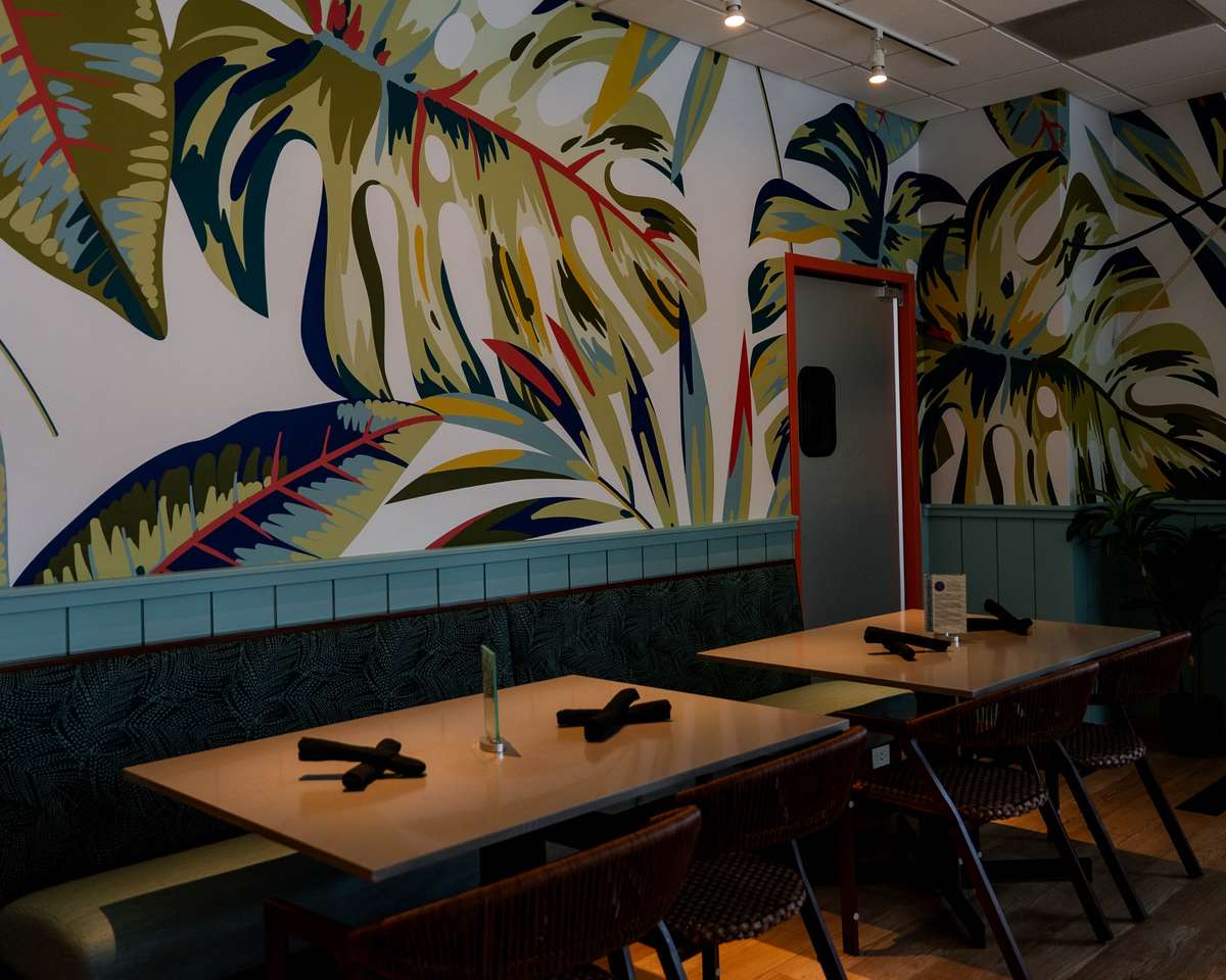 Restaurant booth seating area with a tropical mural on the wall.