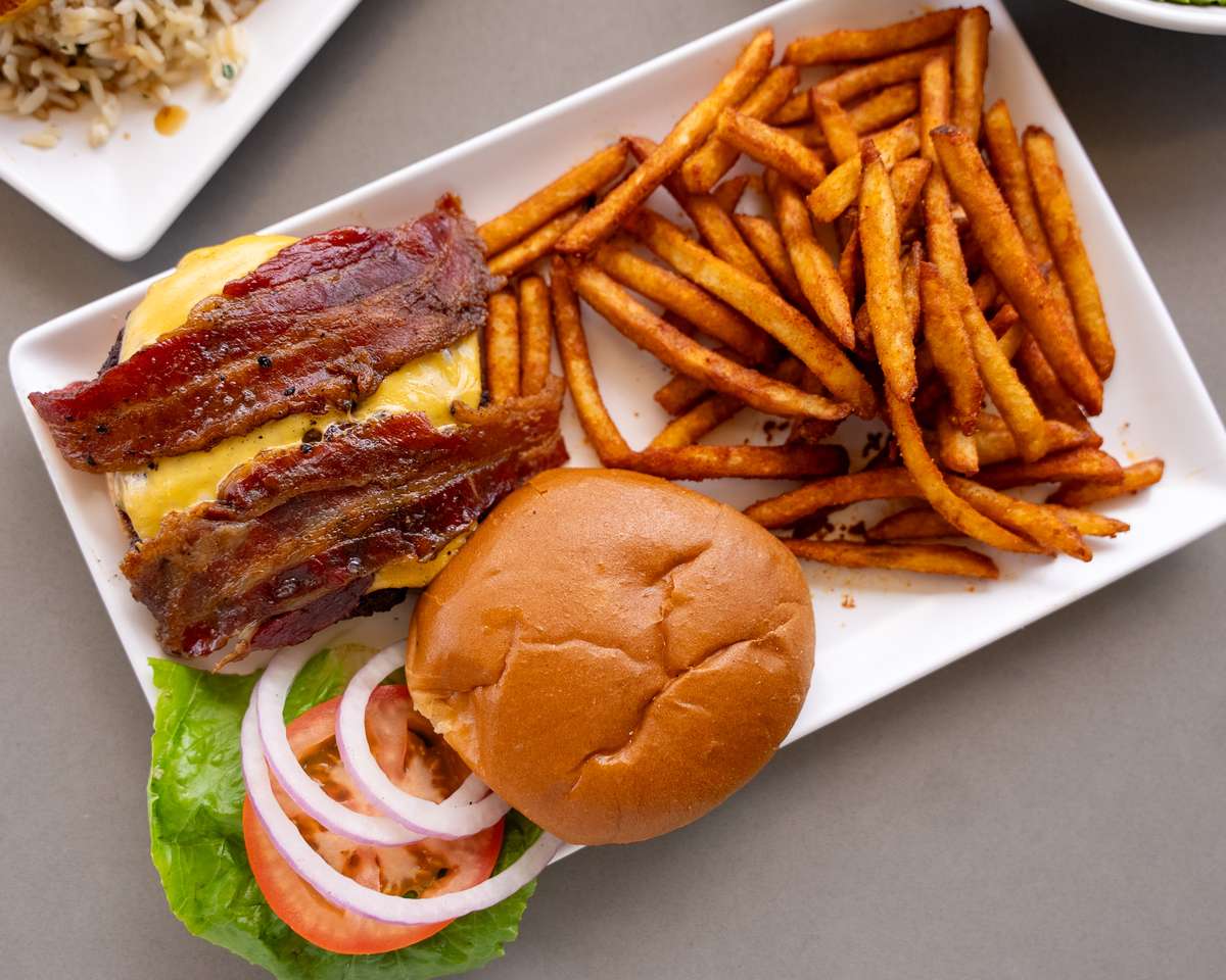 Burger on a bun served with fries on a white plate.