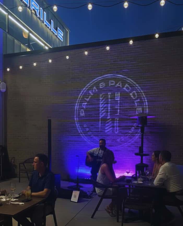 image of musician playing outside on the patio with listeners sitting at tables