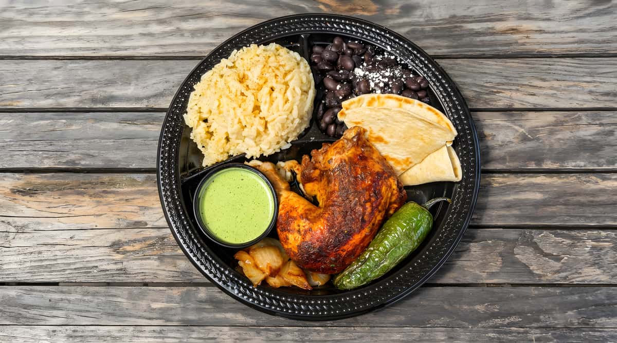 Roasted chicken plate with rice, beans, plantains, and green sauce.