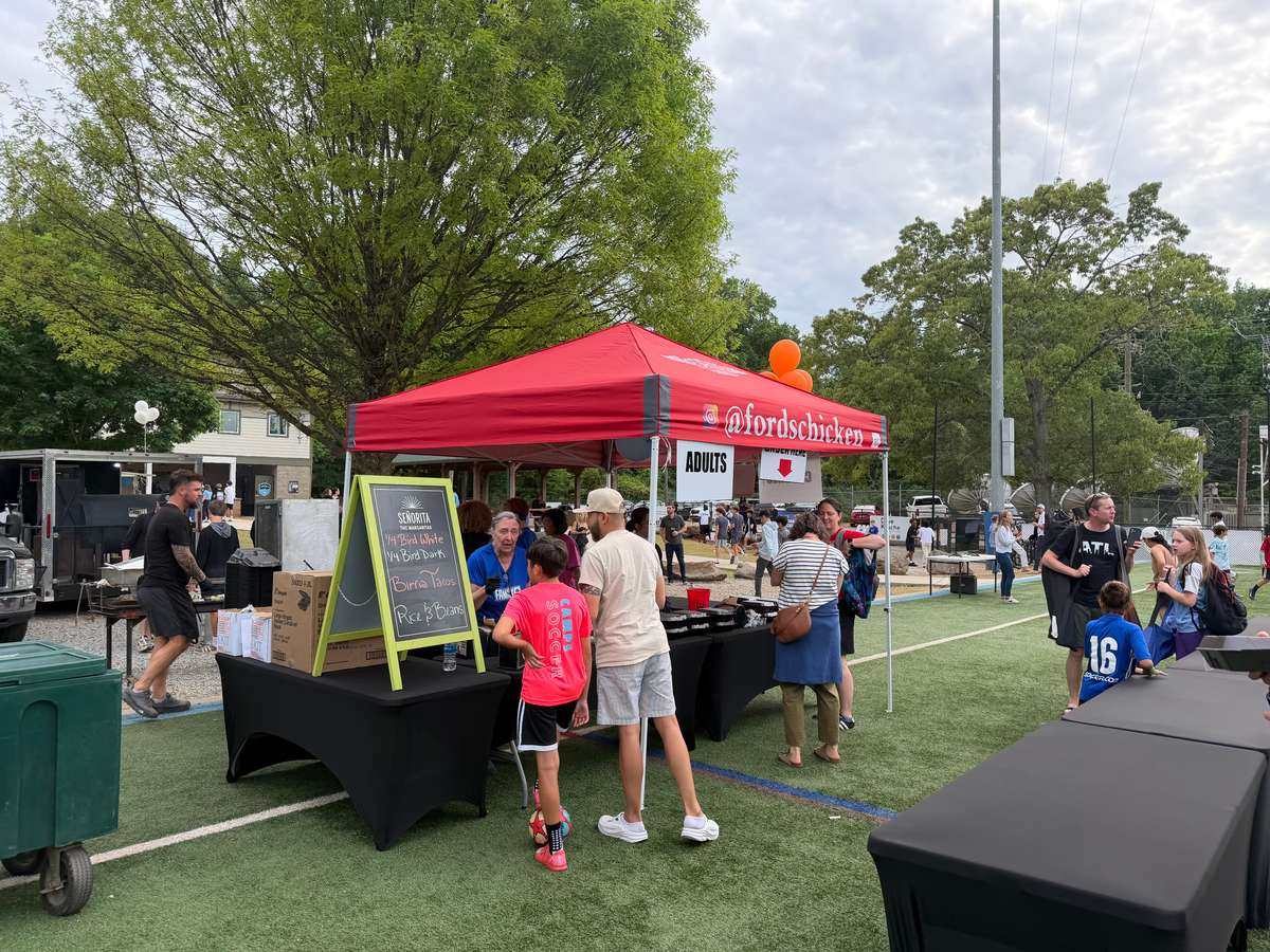Outdoor food event with people gathered around vendor tents and tables.