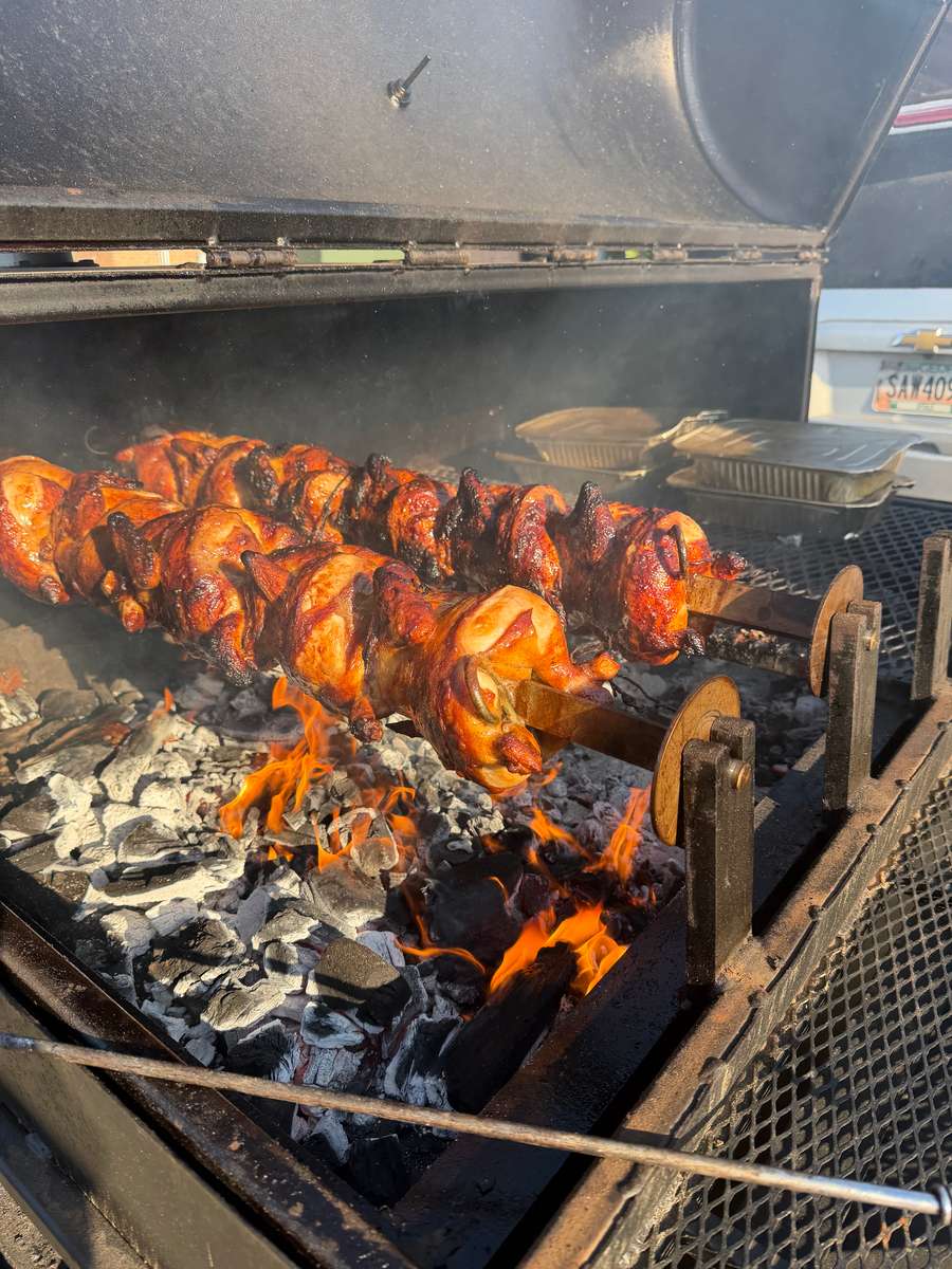 Whole chickens roasting on a rotisserie over open flames.