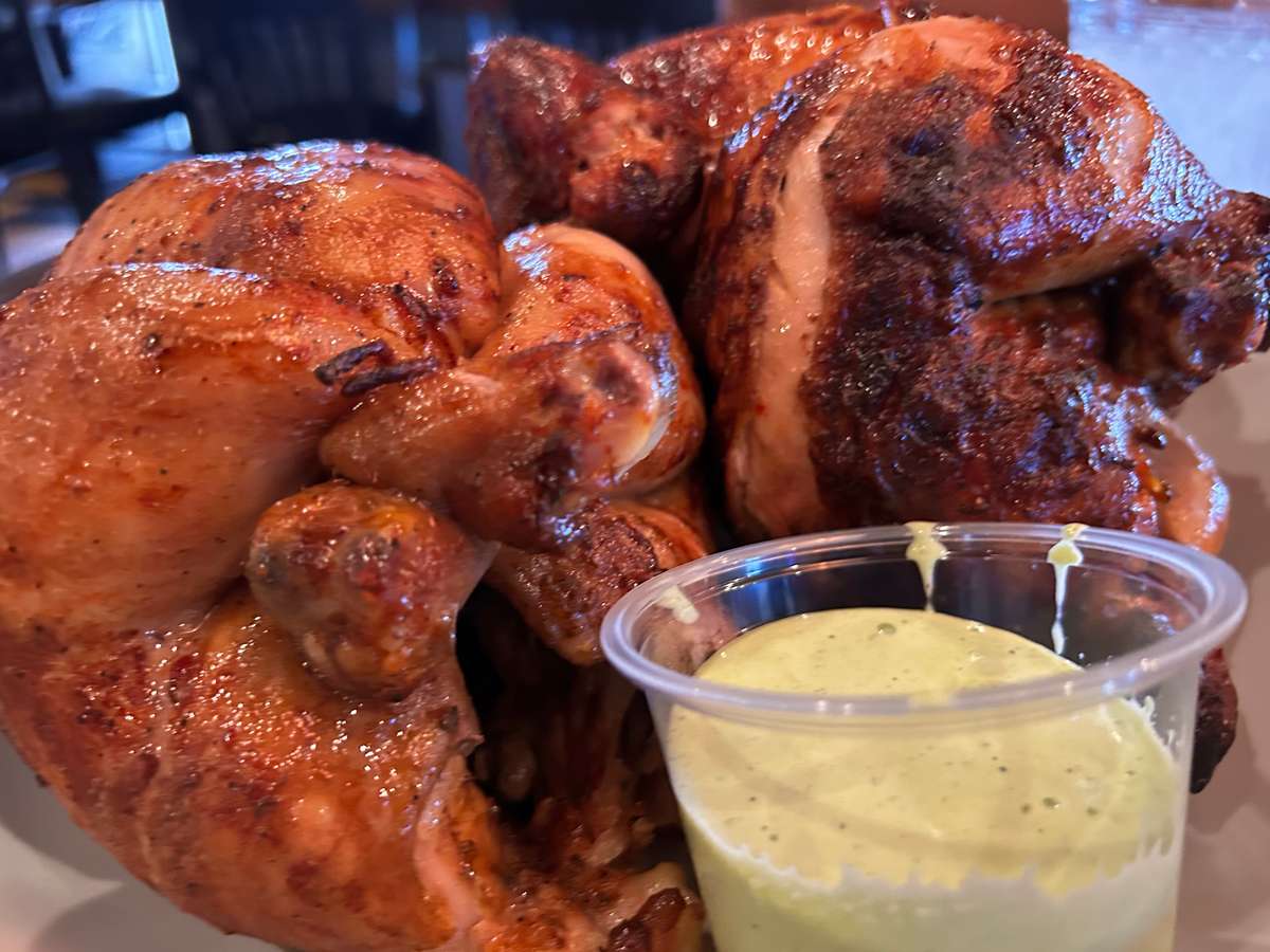 Roasted chicken served with a side of creamy dipping sauce.