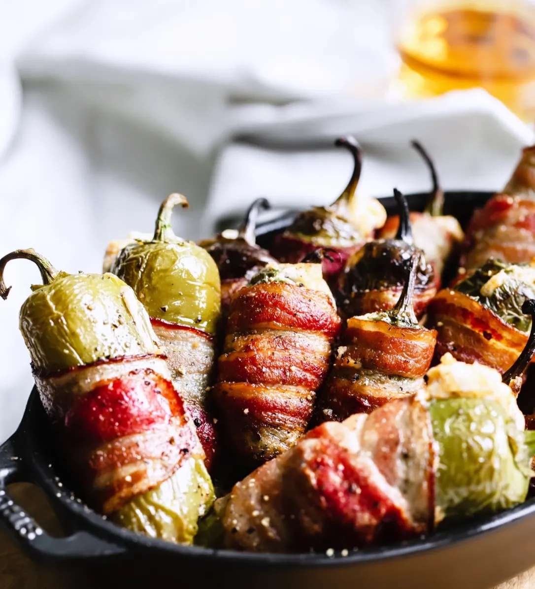 Close-up of bacon-wrapped jalapeño poppers stuffed with creamy cheese, served hot in a cast iron skillet—perfect for a spicy appetizer or game day snack at a Tex-Mex or barbecue restaurant.