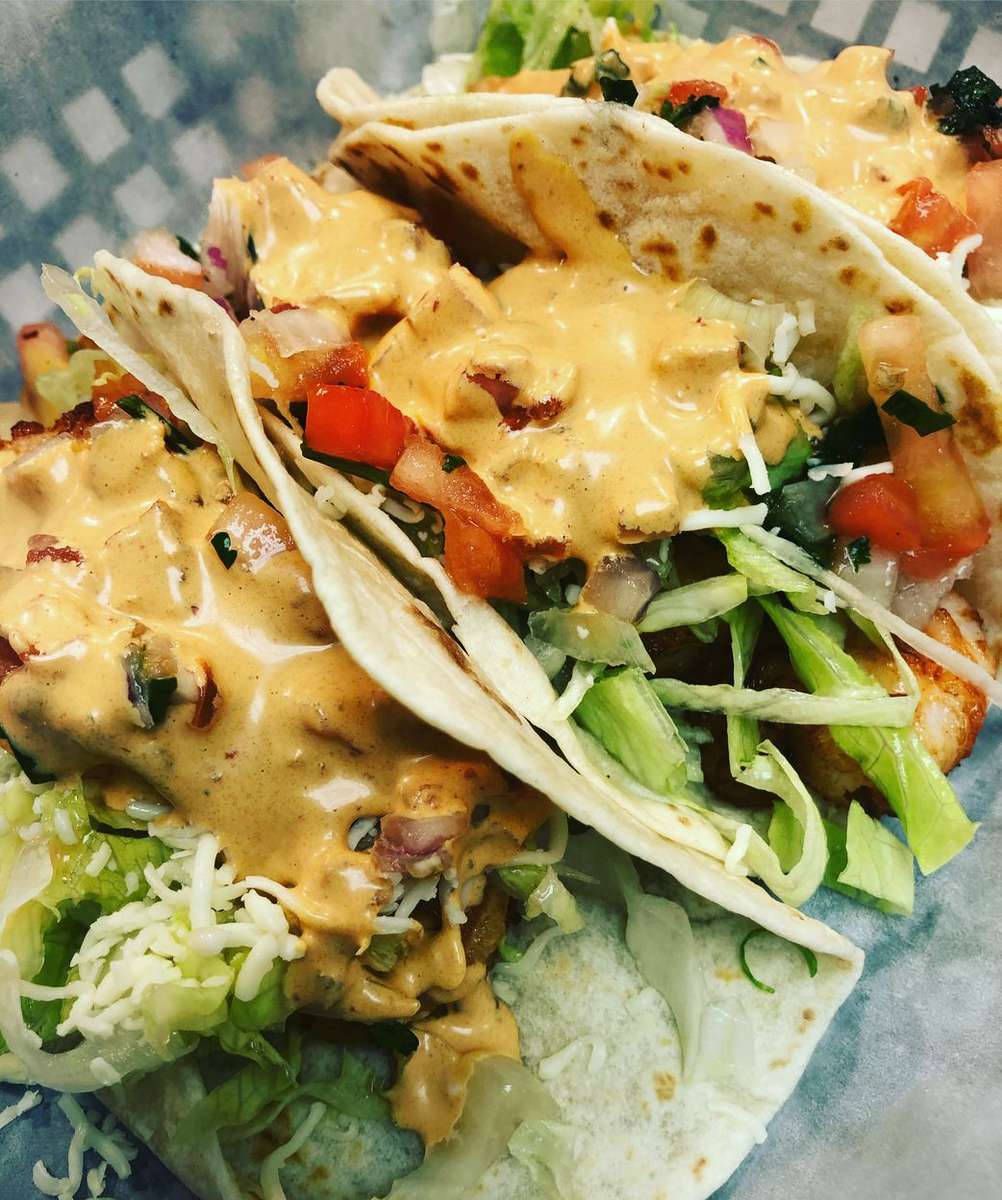 Soft flour tortillas filled with crispy fried fish, shredded lettuce, pico de gallo, and topped with a creamy chipotle sauce—freshly made fish tacos ideal for coastal or Baja-style Mexican cuisine.