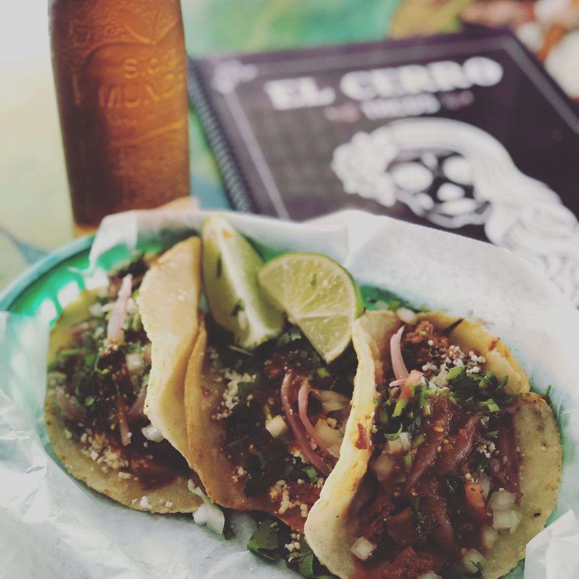 Trio of classic Mexican street tacos topped with chopped onions, cilantro, and crumbled cheese, served with lime wedges and a cold beer—ideal for taco Tuesday or casual taqueria menus.