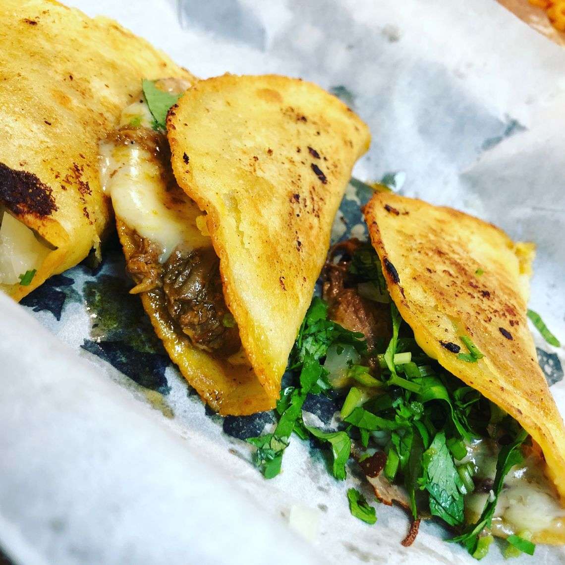 Golden crispy birria tacos filled with slow-cooked beef, melted cheese, cilantro, and onions—served street-style on parchment paper, perfect for authentic Mexican comfort food.