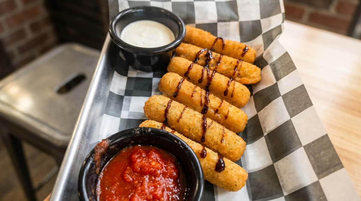 Crispy breaded mozzarella sticks served with marinara sauce and creamy ranch dipping sauce, finished with a balsamic glaze drizzle.