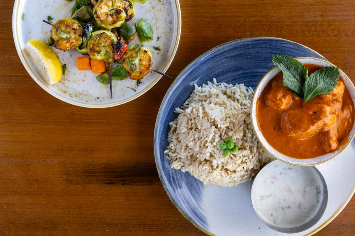 A bowl of mixed grilled vegetables and paneer alongside a serving of rice and Indian curry sauce.