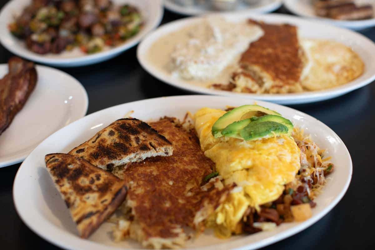 Southwestern-style omelette topped with fresh avocado slices, served with crispy hash browns, grilled toast, and sautéed breakfast vegetables — a hearty and colorful American diner breakfast plate.