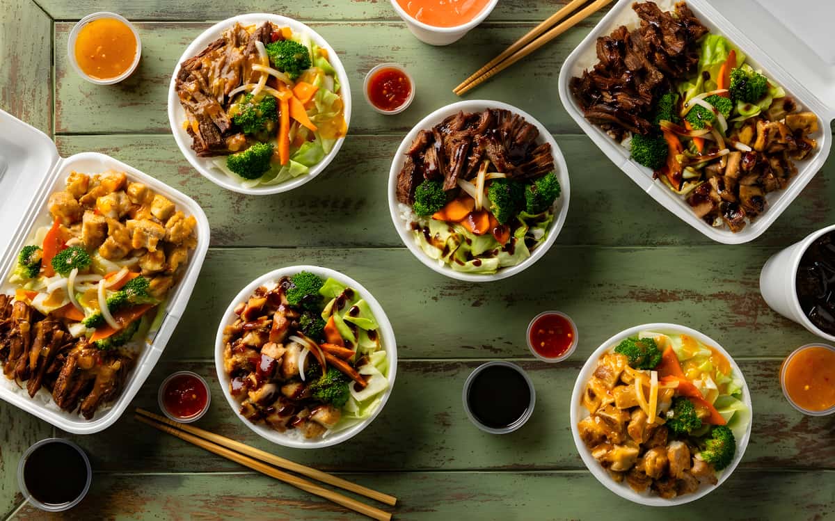 Assorted Asian-style grilled chicken and beef bowls with broccoli, carrots, cabbage, dipping sauces, and chopsticks