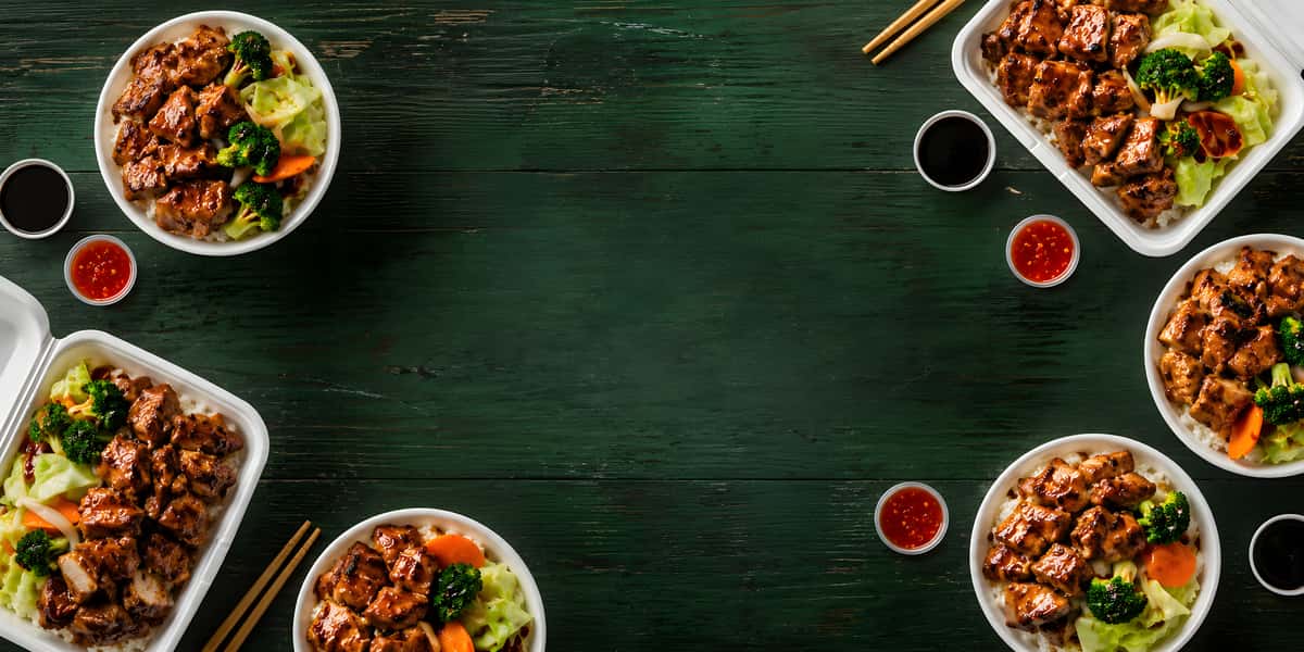 Asian-style grilled chicken rice bowls with broccoli, cabbage, carrots, dipping sauces, and chopsticks