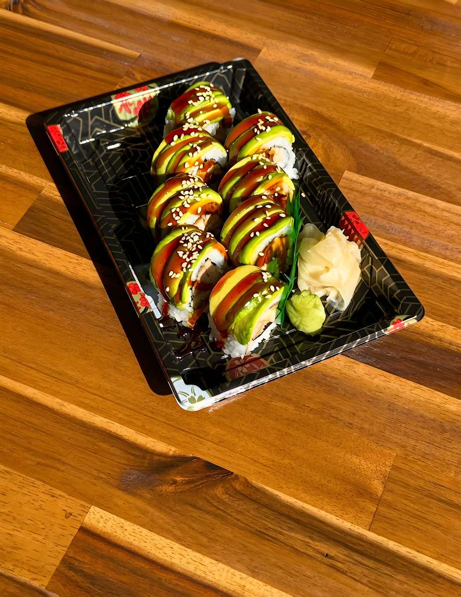 Avocado-topped sushi rolls drizzled with teriyaki sauce and sesame seeds, served with pickled ginger and wasabi