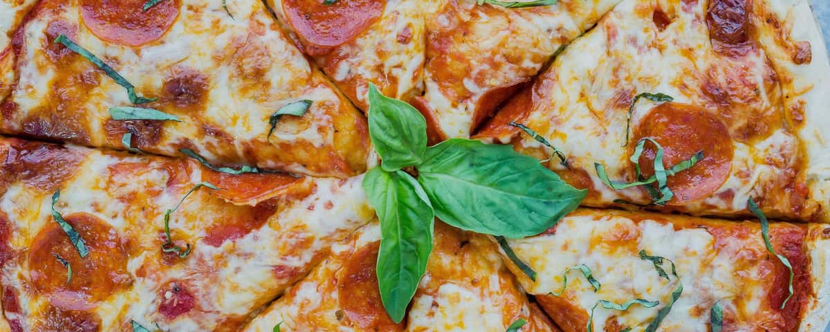 Cheesy pizza with tomato slices and a rocket leaf garnish