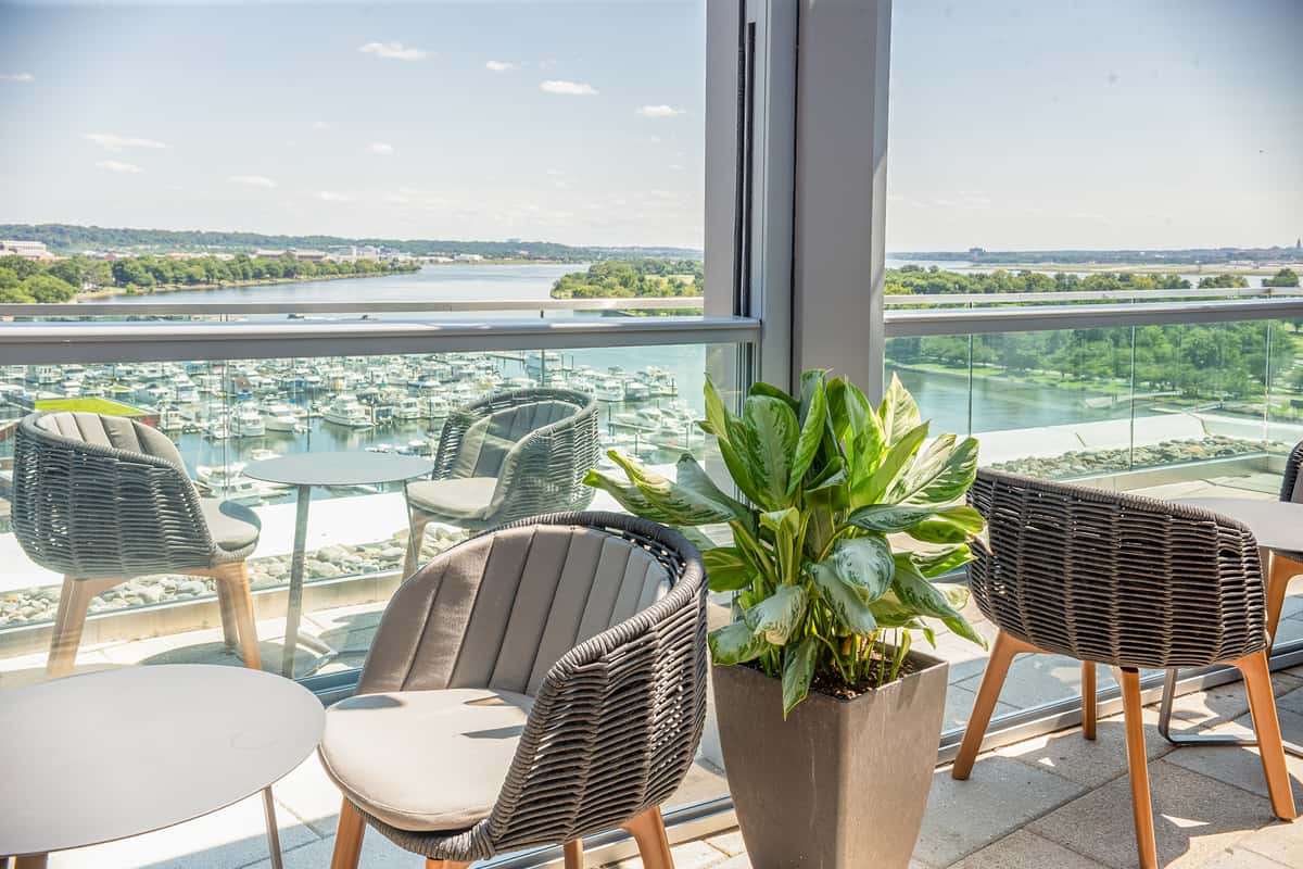 Rooftop patio seating area with woven chairs and a potted plant, overlooking a waterfront view at a restaurant