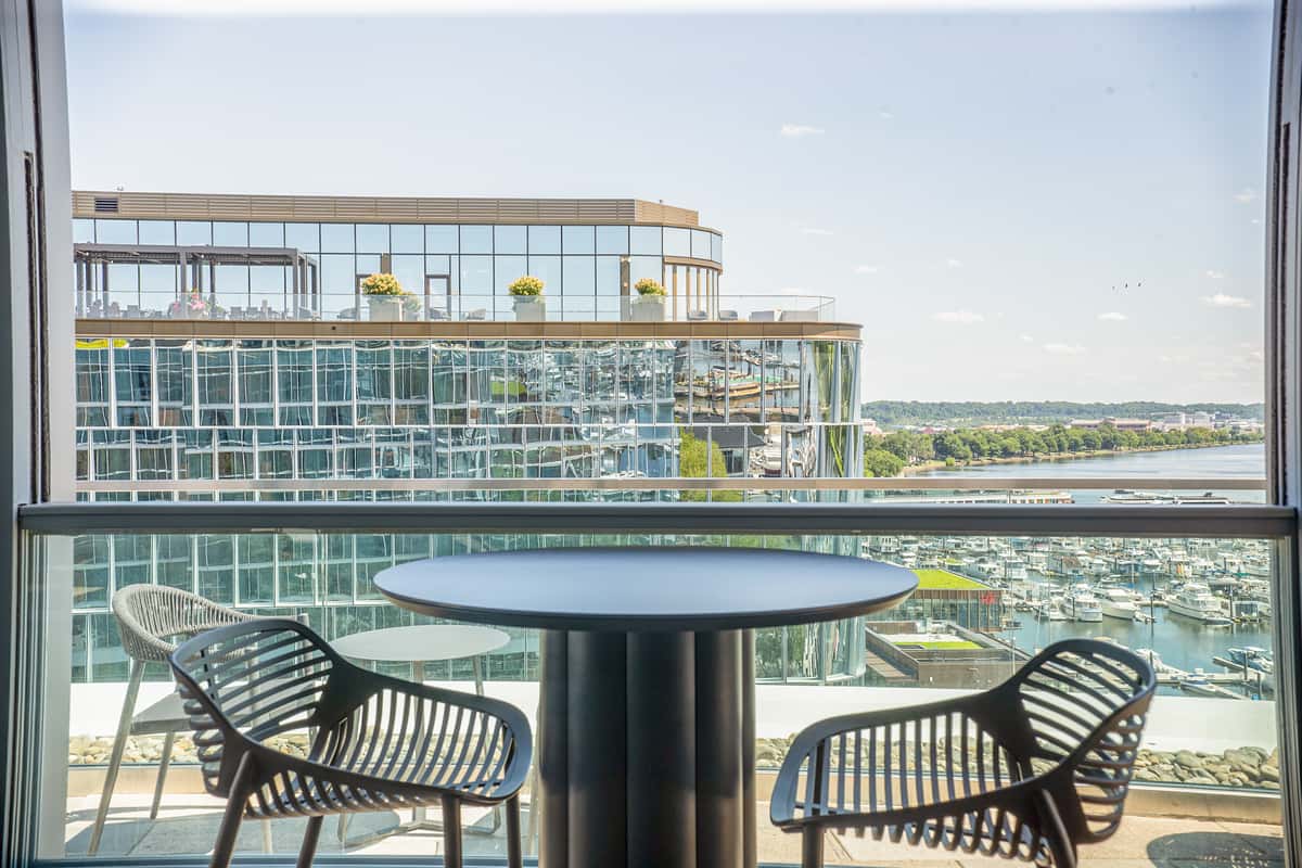 Rooftop patio seating area with a round dark table and woven chairs, overlooking a waterfront view at a restaurant