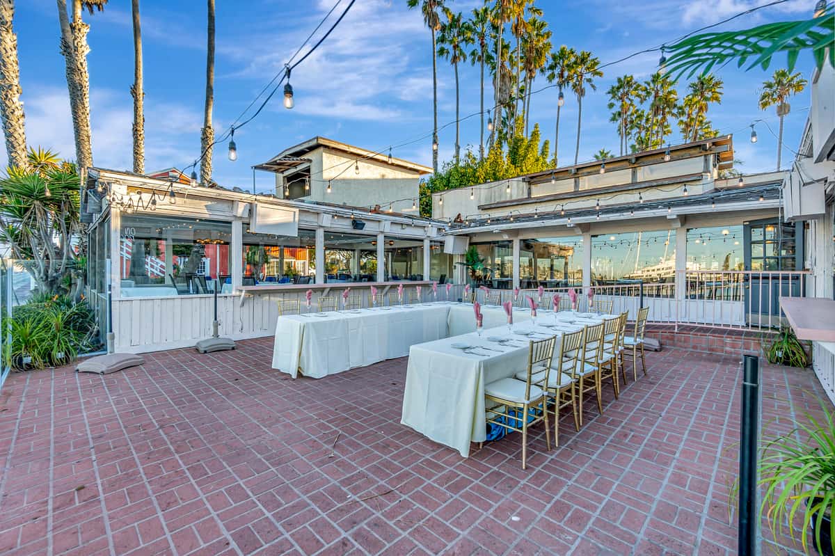 Outdoor waterfront event patio with long banquet tables, string lights, and tropical palm trees for private dining and celebrations
