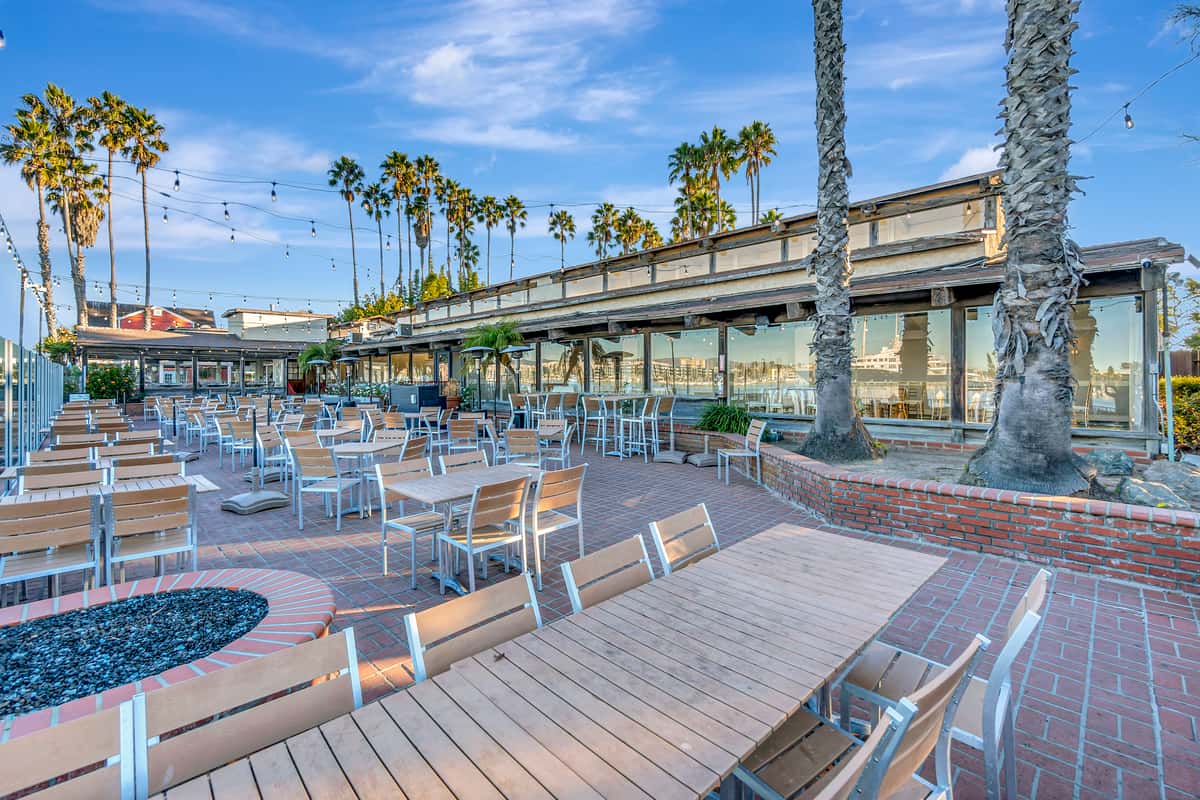 Spacious waterfront patio dining area with palm trees, marina views, fire pits, and outdoor seating at a coastal restaurant