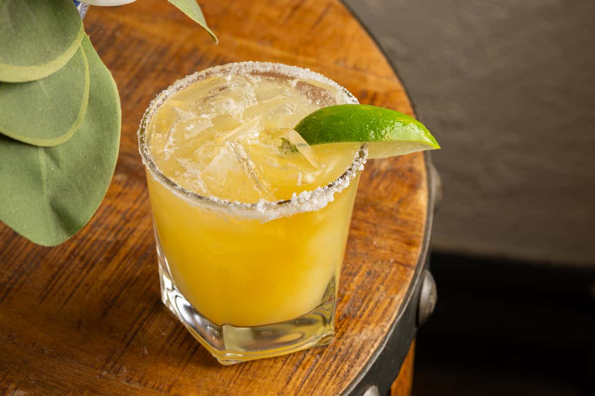 Fresh citrus margarita with a salted rim and lime garnish served over ice on a rustic wooden table