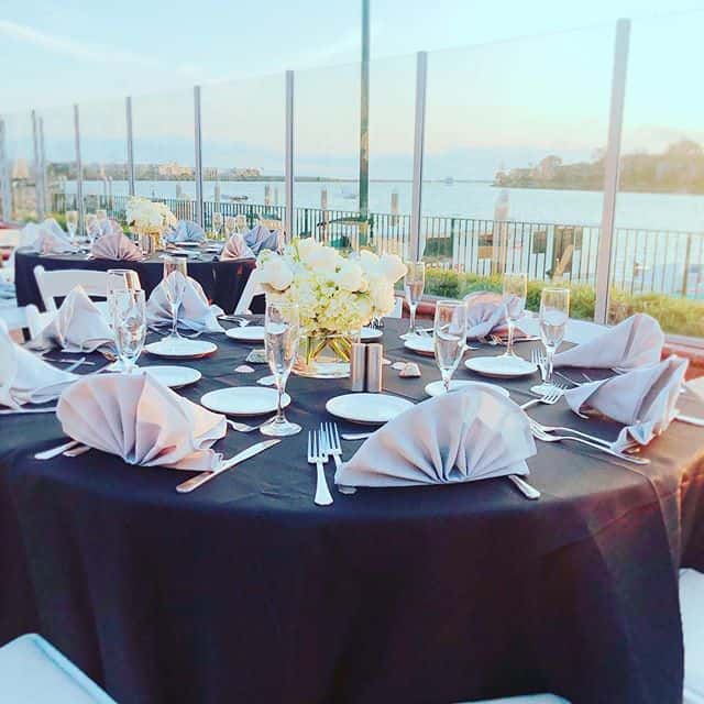 Elegant waterfront dining table with black linens, folded napkins, and marina views for upscale private events and wedding receptions