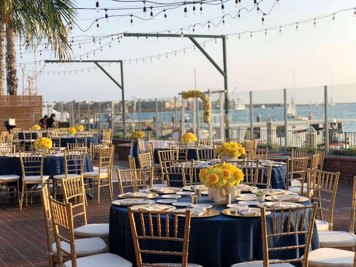 Outdoor waterfront wedding reception setup with navy table linens, string lights, and marina sunset views