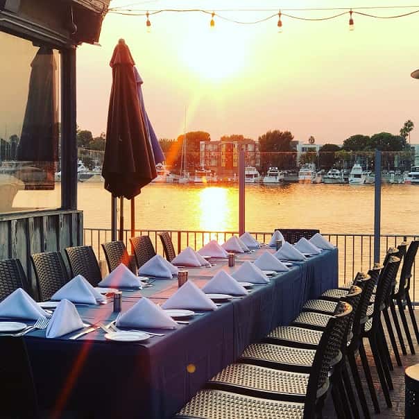 Sunset waterfront dining table setup with elegant place settings and marina views on a private outdoor patio