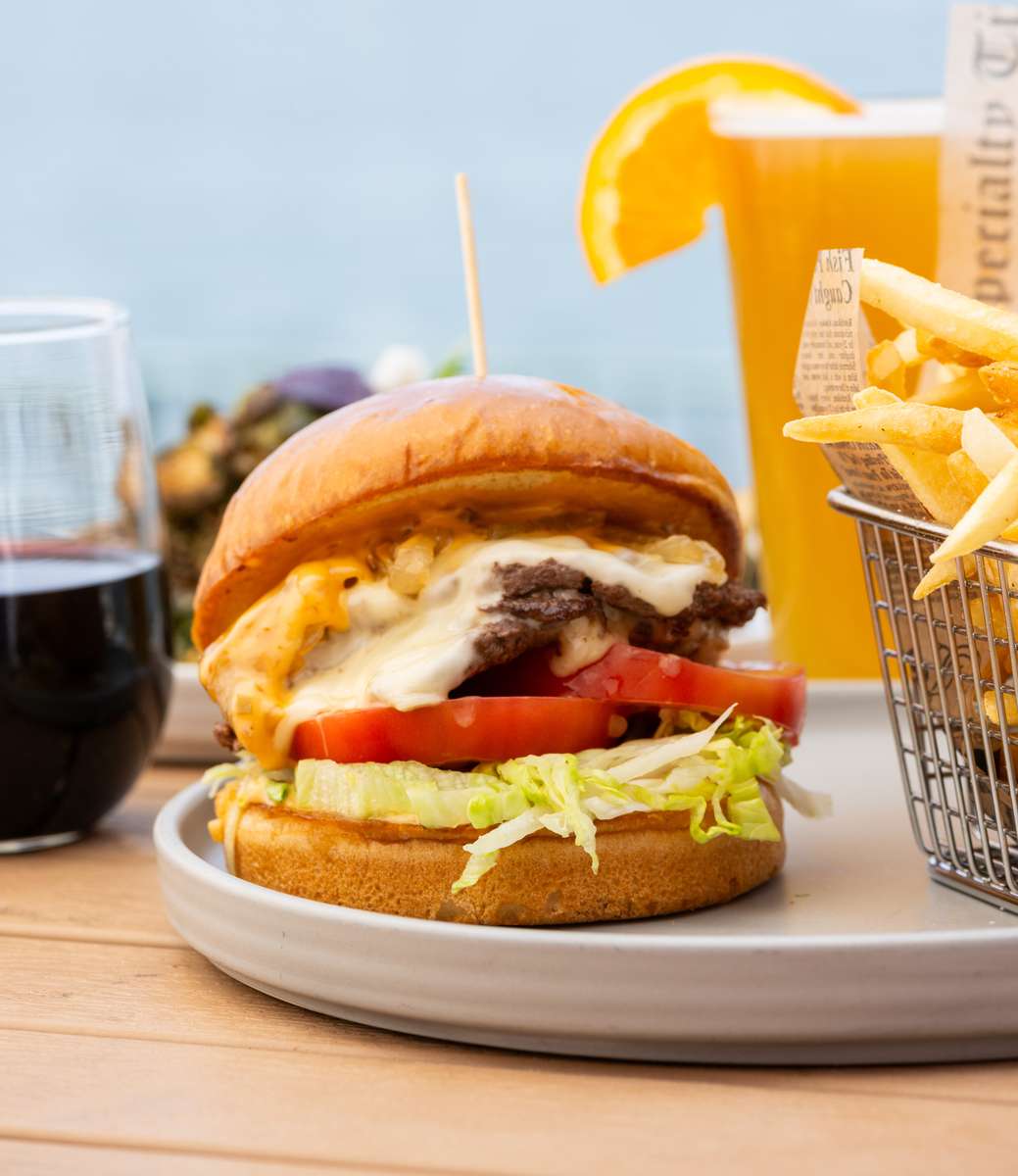 Juicy cheeseburger with lettuce, tomato, melted cheese, and crispy fries served with cocktails at a waterfront restaurant