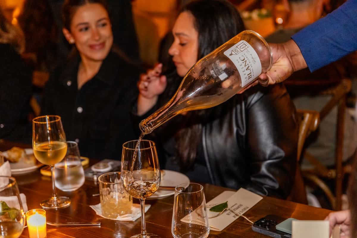 Server pouring white wine into a glass during a warm restaurant dinner service