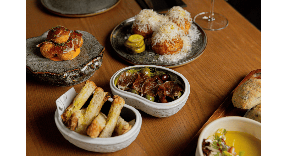 Assortment of gourmet appetizers including croquettes, cured meats, olives, and toasted bread at a luxury dining restaurant.