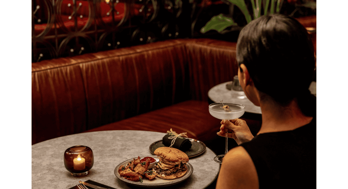 Guest enjoying a cocktail and gourmet burger at a candlelit booth in an upscale Las Vegas restaurant.
