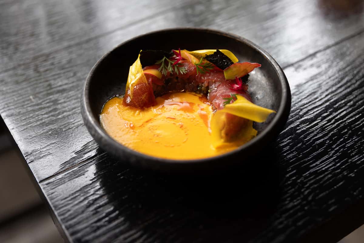 Fine dining dish with yellow sauce, glazed ingredients, and artistic garnish
