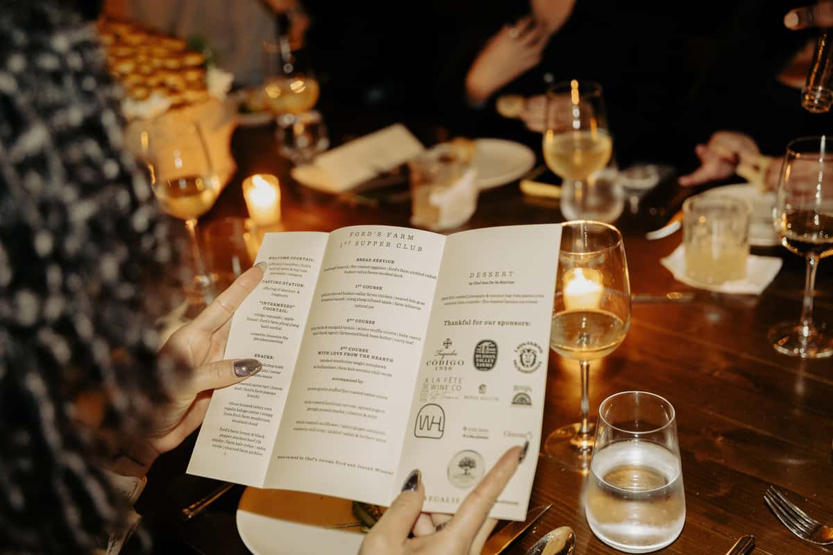 Guest reading a tasting menu at a candlelit supper club table during an upscale dining experience