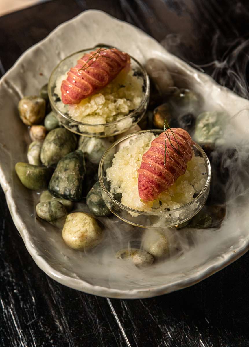 Gourmet granita dessert with pink fruit topping served over stones with dry ice smoke